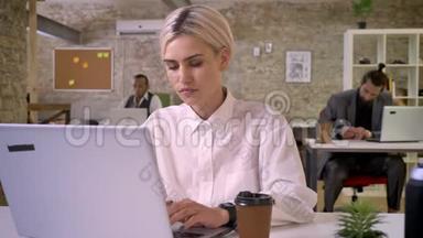 年轻快乐的女商人正在办公室里用笔记本电脑<strong>打字</strong>，喝着咖啡，同事们正在与科技建立<strong>联系</strong>